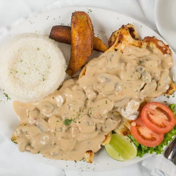 Colombian chicken in mushroom sauce with rice, fried plantains, lime, and tomatoes.