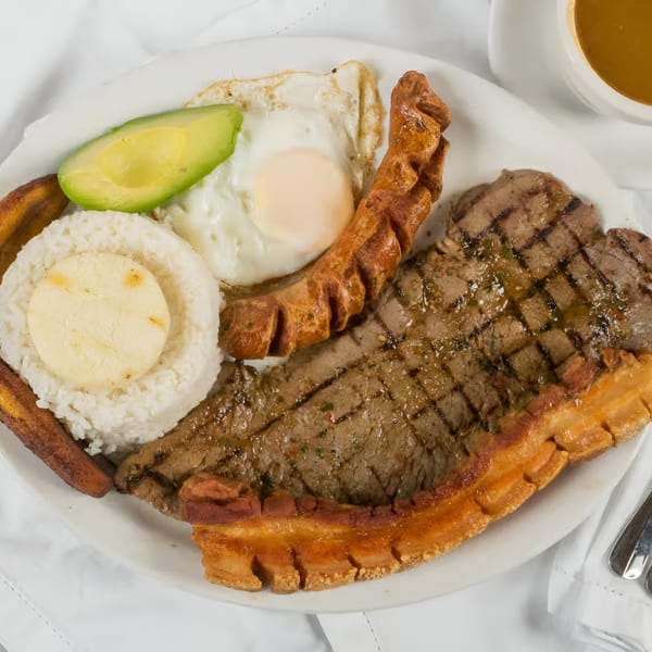 A Colombian breakfast with grilled steak, fried egg, rice, avocado, plantain, and chicharrón.