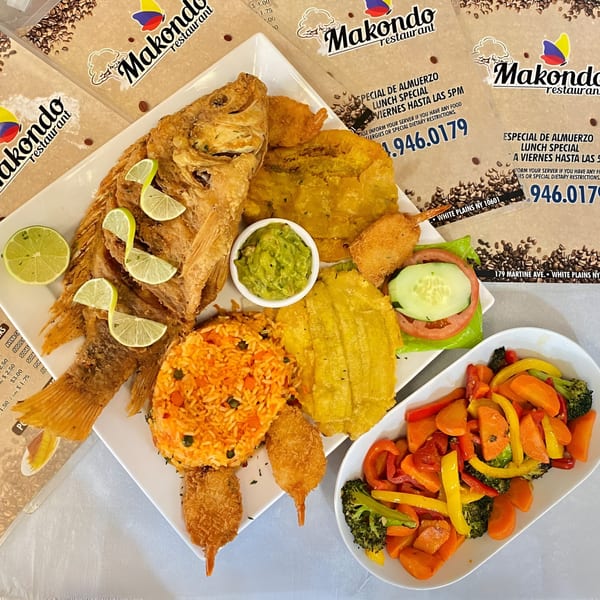 A Colombian fried whole fish with lime, rice, plantains, shrimp, guacamole, and vegetables.