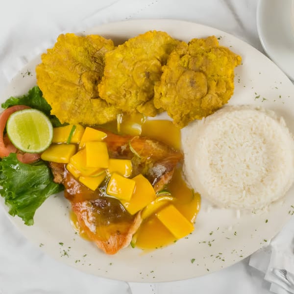 Colombian dish with mango-topped fish, tostones, white rice, and a side salad with lime.
