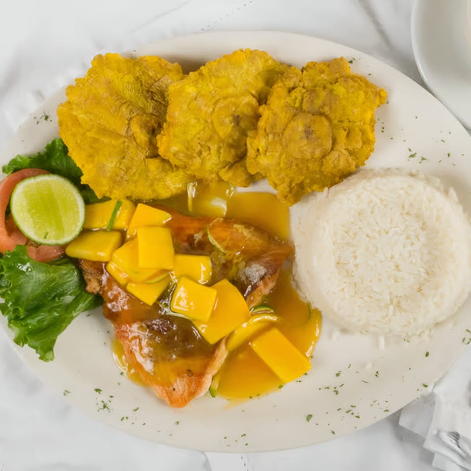 Colombian dish with mango-topped fish, tostones, white rice, and a side salad with lime.