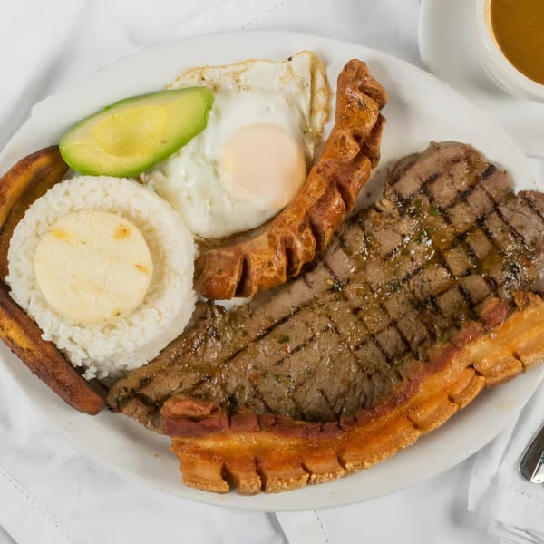 A Colombian bandeja paisa with steak, fried egg, avocado, rice, plantain, and chicharron.