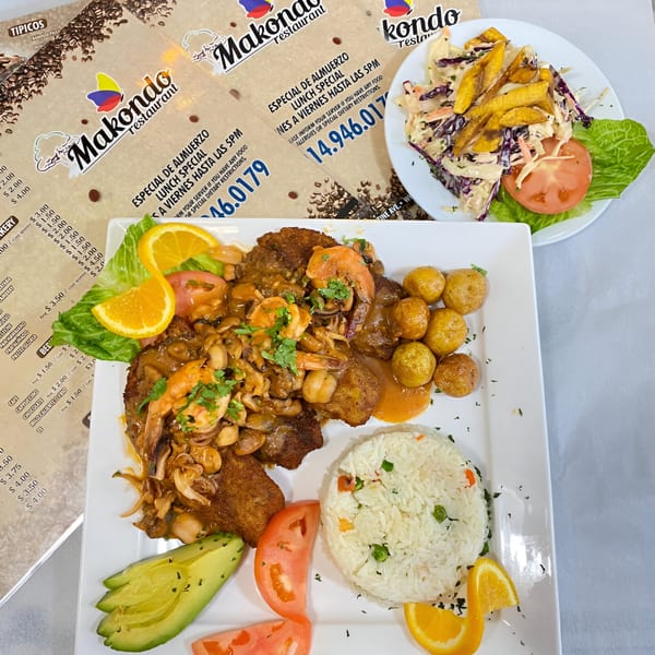 A Colombian meal with shrimp, mushrooms, potatoes, rice, avocado, and tomatoes, with menus in the background.