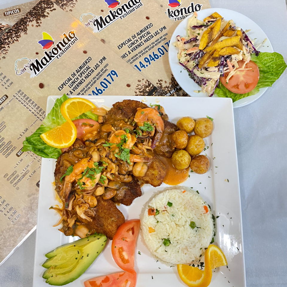 A Colombian meal with shrimp, mushrooms, potatoes, rice, avocado, and tomatoes, with menus in the background.