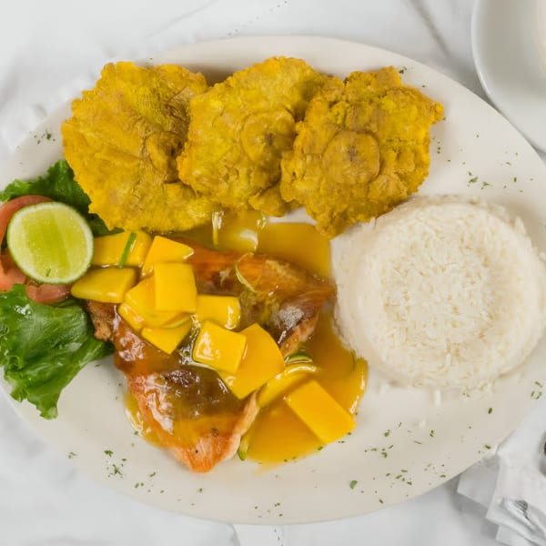 Colombian dish with fish in mango sauce, white rice, fried plantains, and a side salad.